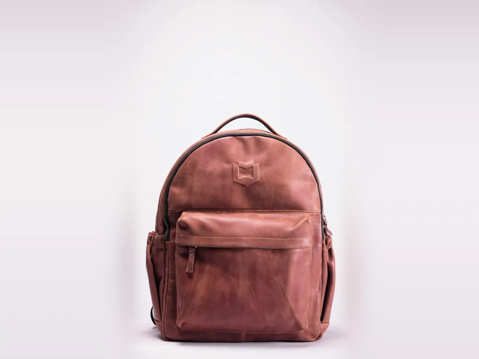 Brown leather backpack standing on a white surface