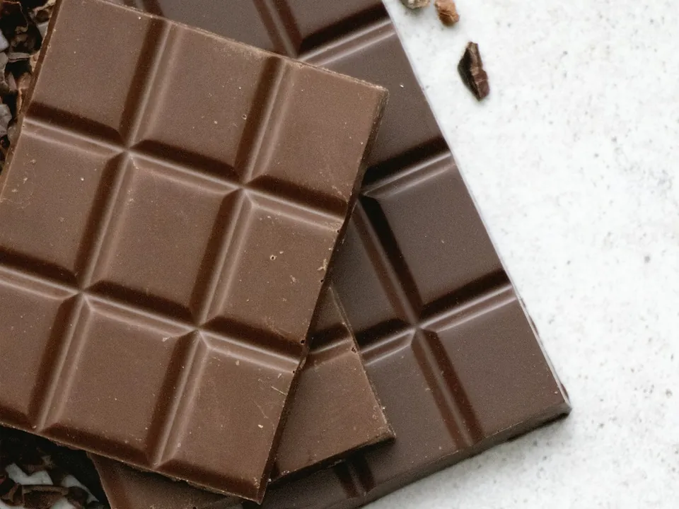 Milk chocolate bars stacked with cocoa nibs on a white table