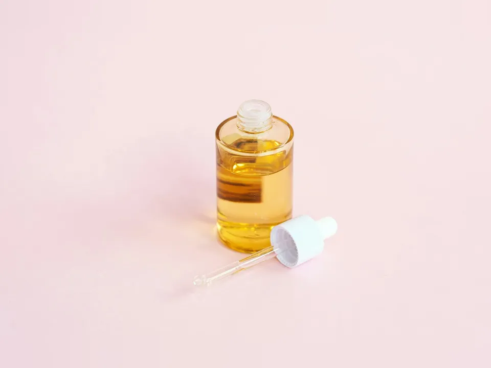 Glass serum bottle with amber oil and a dropper on a pale pink surface