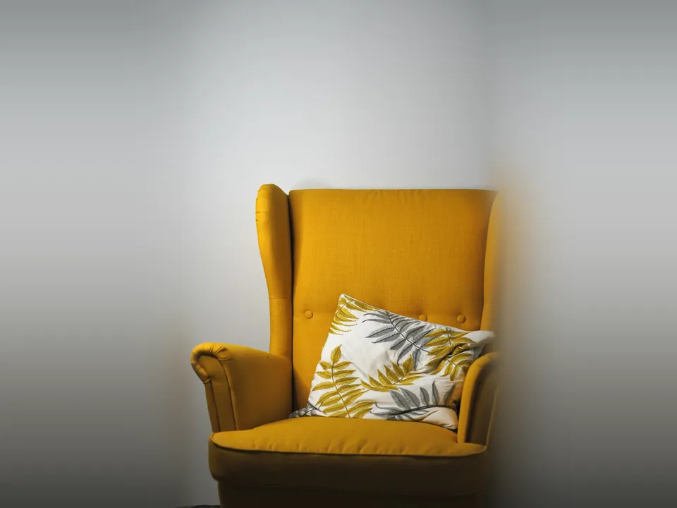 Mustard yellow wingback armchair with a patterned cushion against a white wall