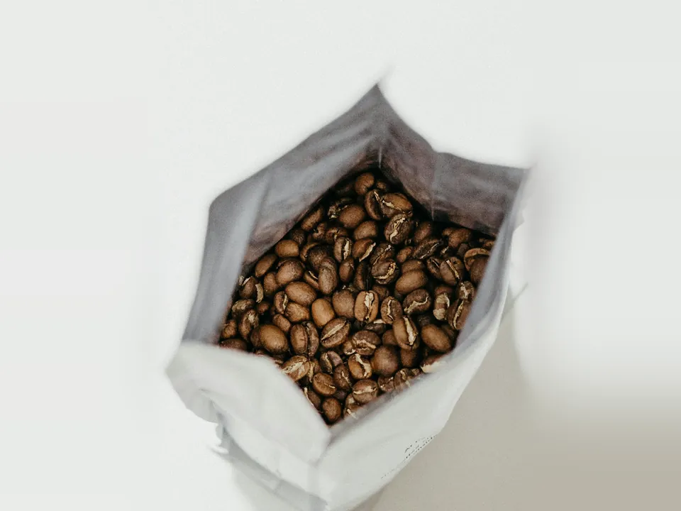 Open plain white bag filled with roasted coffee beans, seen from above